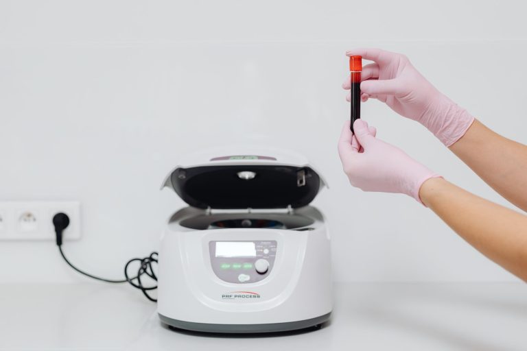 Profissional de saúde, usando luvas, manuseia uma amostra de sangue em uma centrífuga de laboratório.
