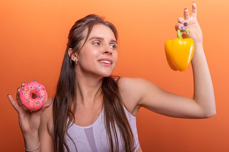 Mulher com roupa esportiva equilibrando uma rosquinha e um pimentão, simbolizando escolhas entre alimentos menos e mais saudáveis.